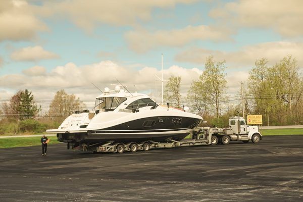 A boat is being towed by a semi truck on a trailer.