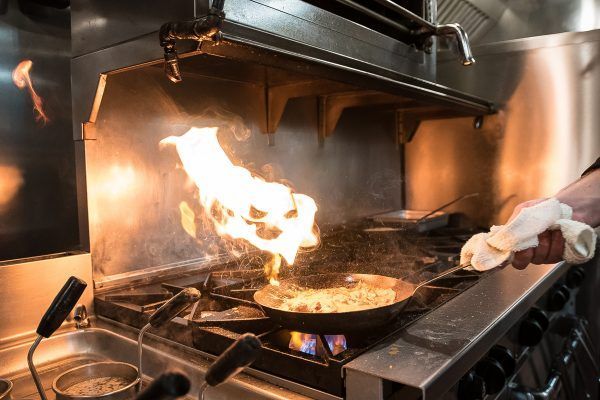 A person is cooking food in a frying pan on a stove.