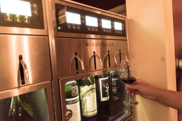 A person is pouring wine into a glass from a wine station