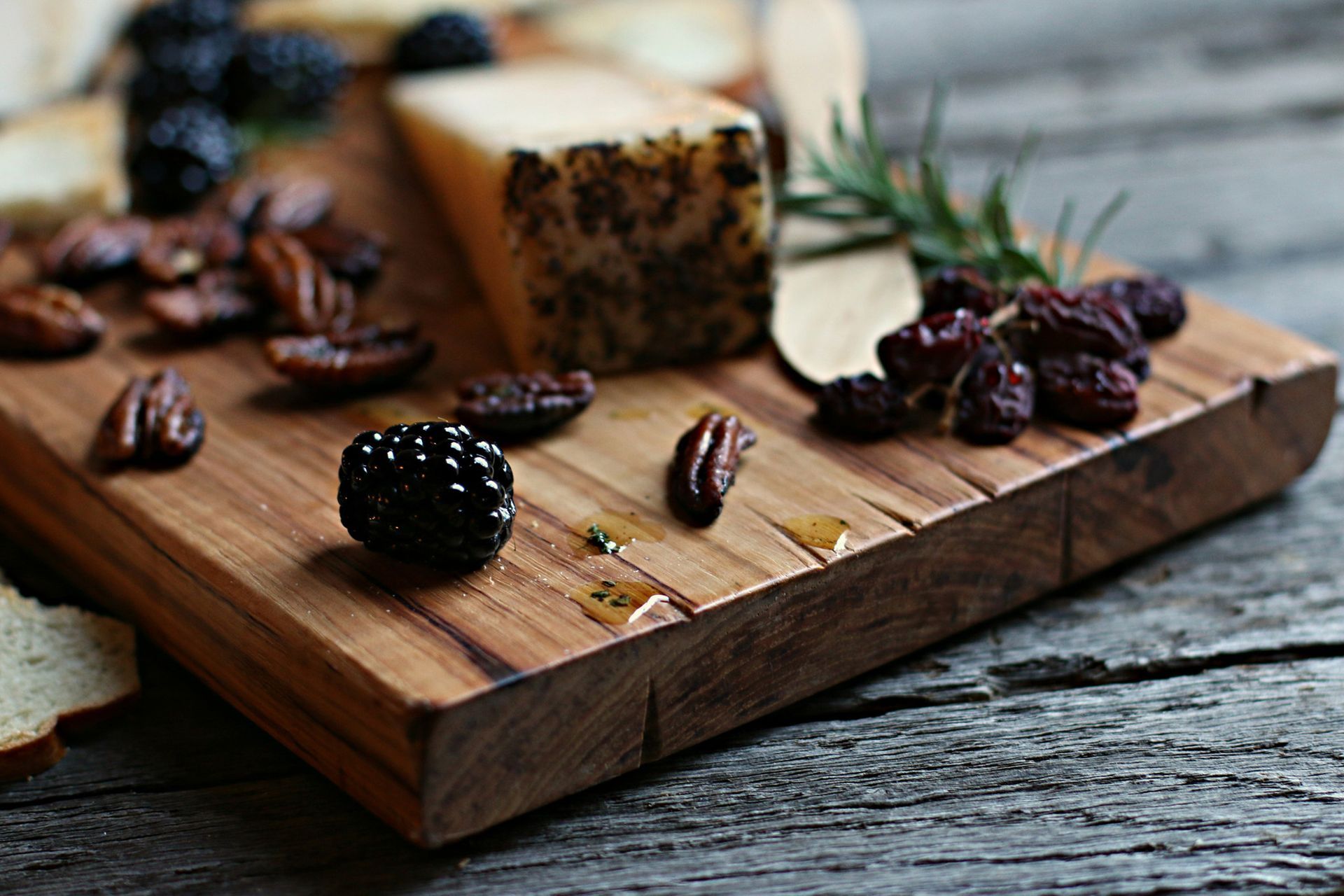 A wooden cutting board with cheese , berries , pecans and bread on it
