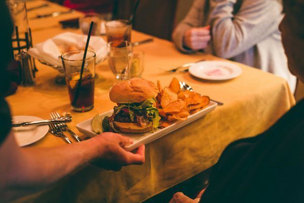 A person is holding a plate of food with a hamburger and chips on it.