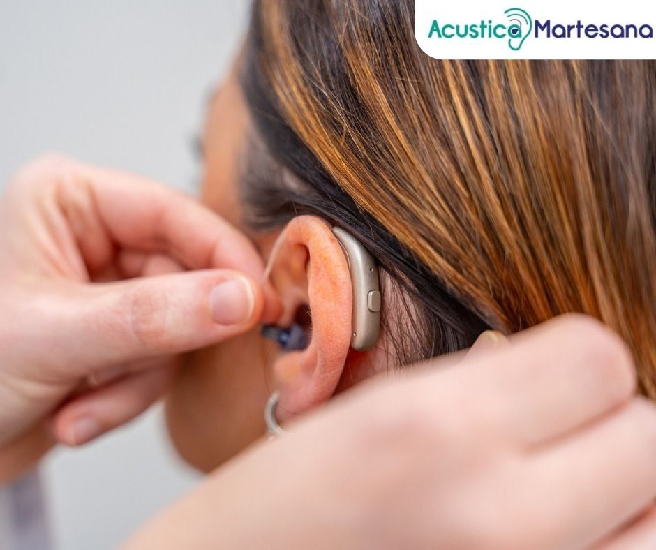 Grembiule di lino beige annodato in vita, con tasca con logo; cucchiaio di legno e ciotola in primo piano.