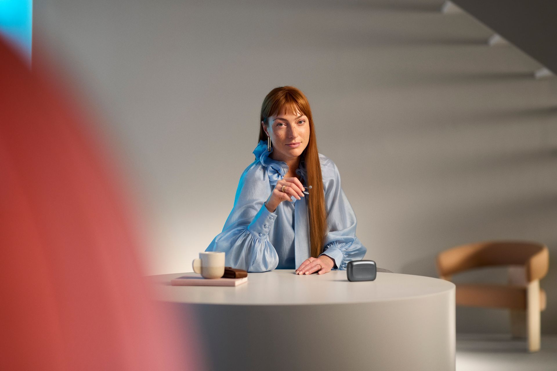 Grembiule di lino beige annodato in vita, con tasca con logo; cucchiaio di legno e ciotola in primo piano.