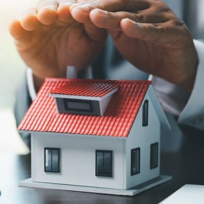 Hands protecting a miniature house with a red roof, symbolizing property insurance.