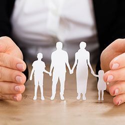 Hands protect a paper family cutout on a wooden surface.