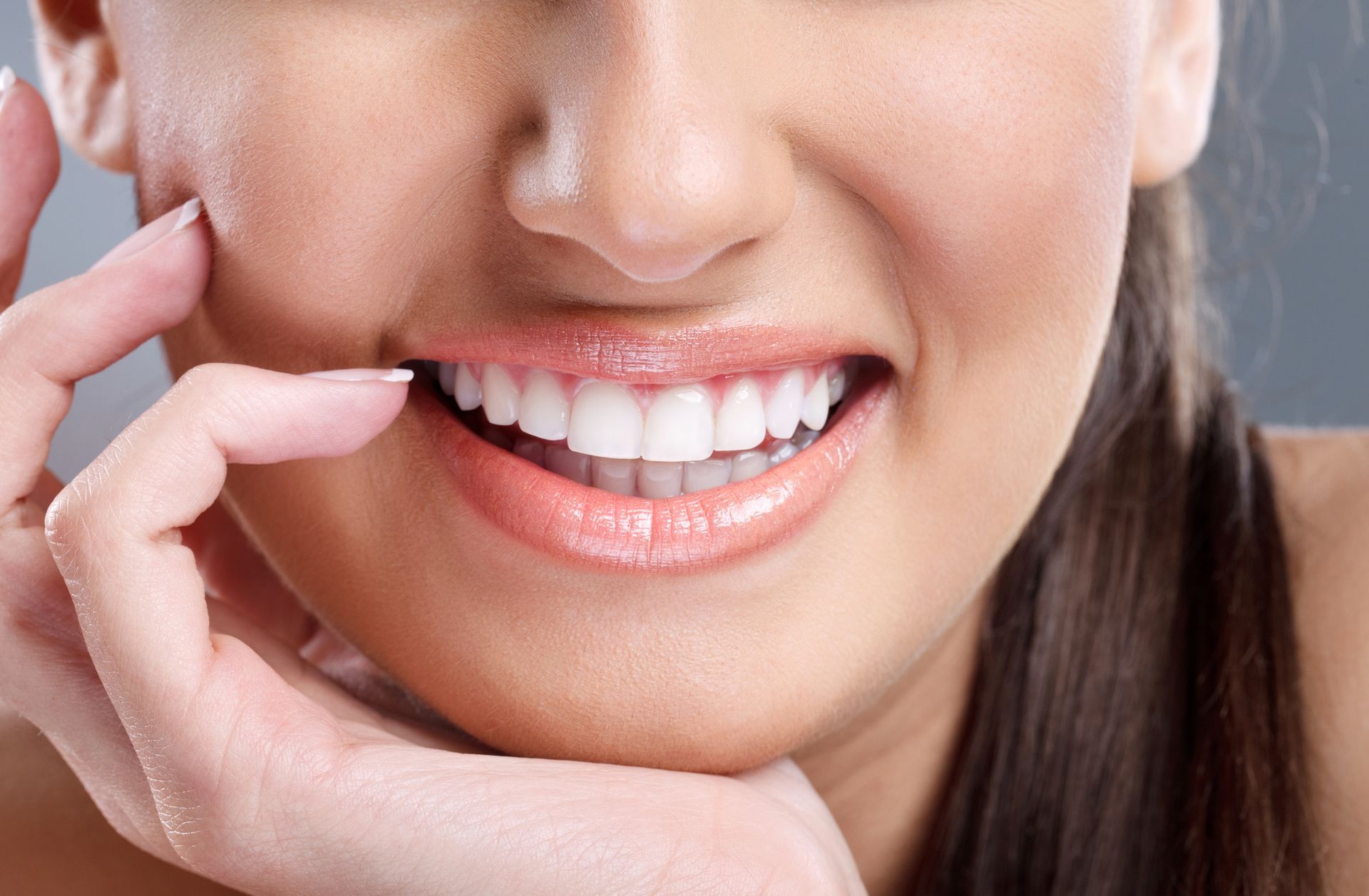 Primo piano di una bocca sorridente con denti bianchi e una mano che tocca la guancia.