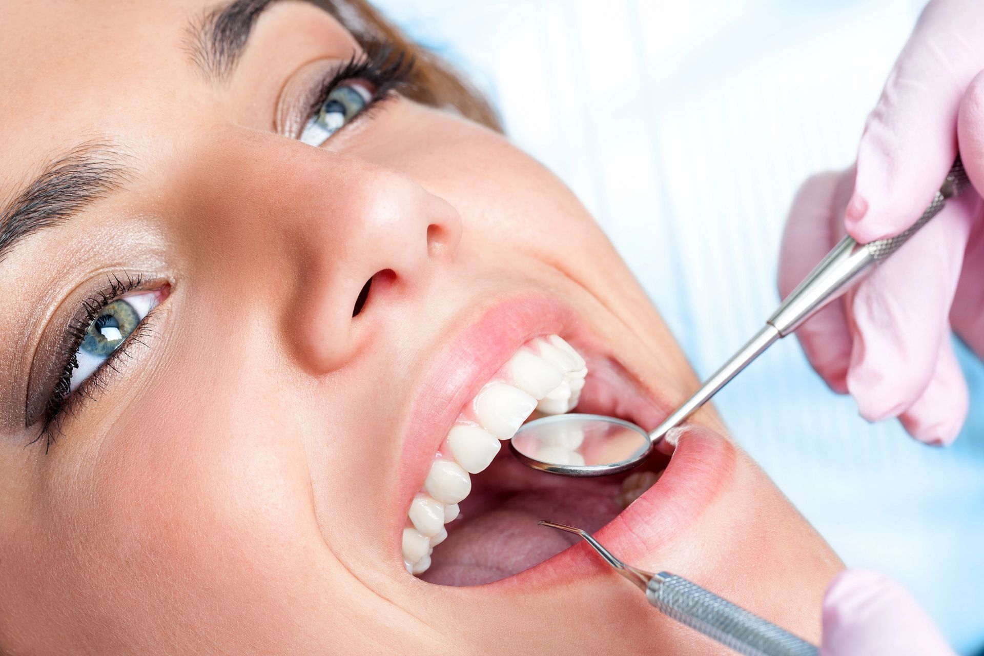 Un dentista esamina la bocca aperta di un paziente con uno specchio e uno strumento, indossando guanti rosa.