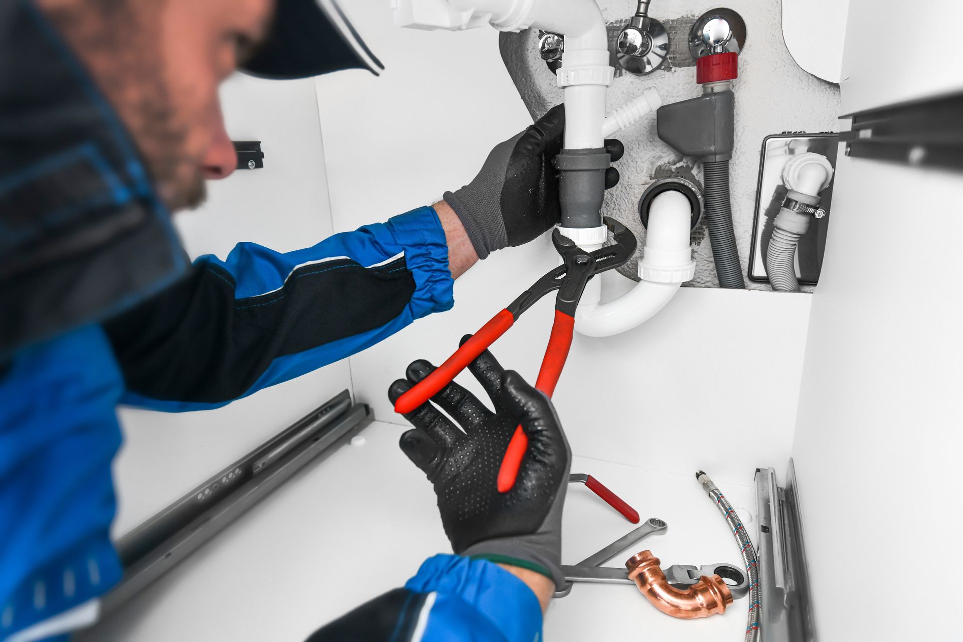 Plumber uses pliers on white pipes under a sink