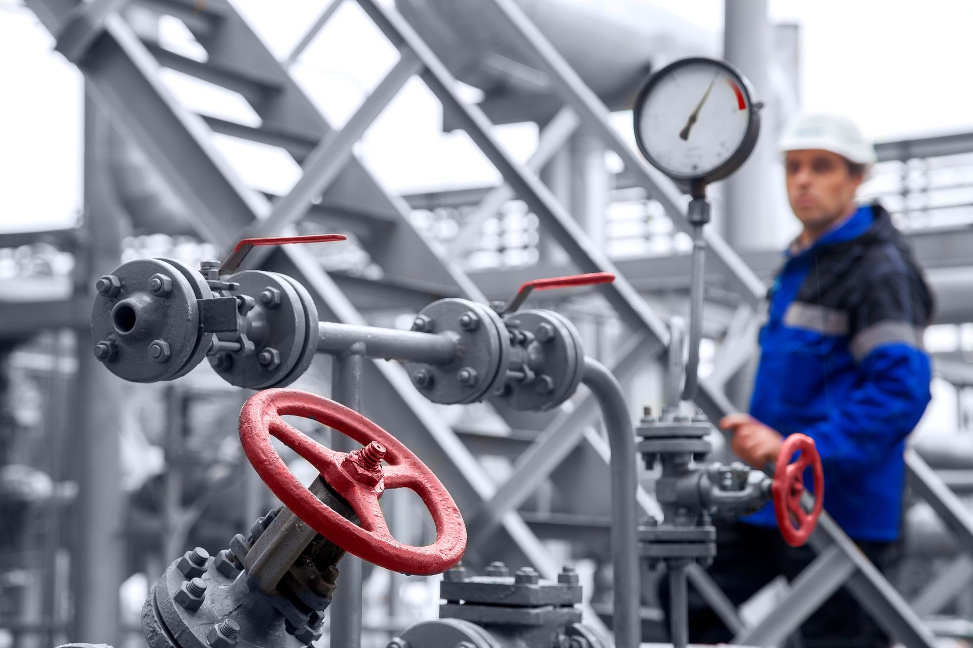 Worker checks gauges on industrial pipes with red valves