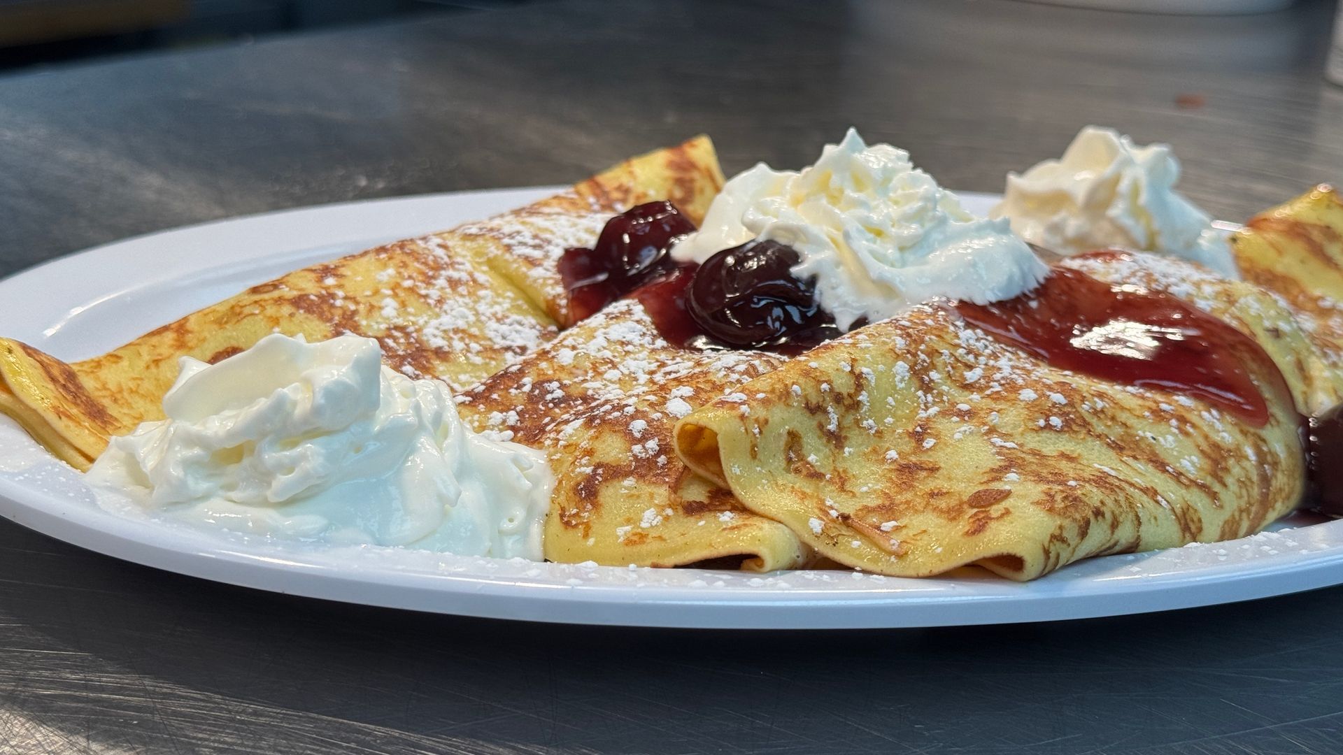 A white plate topped with a crepe with whipped cream and powdered sugar