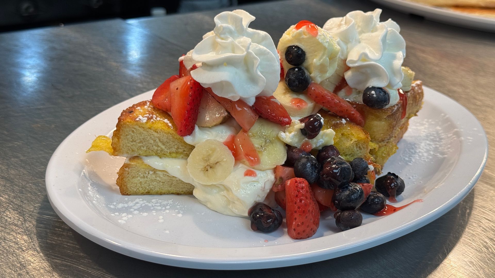 A white plate topped with a piece of french toast with whipped cream and fruit.