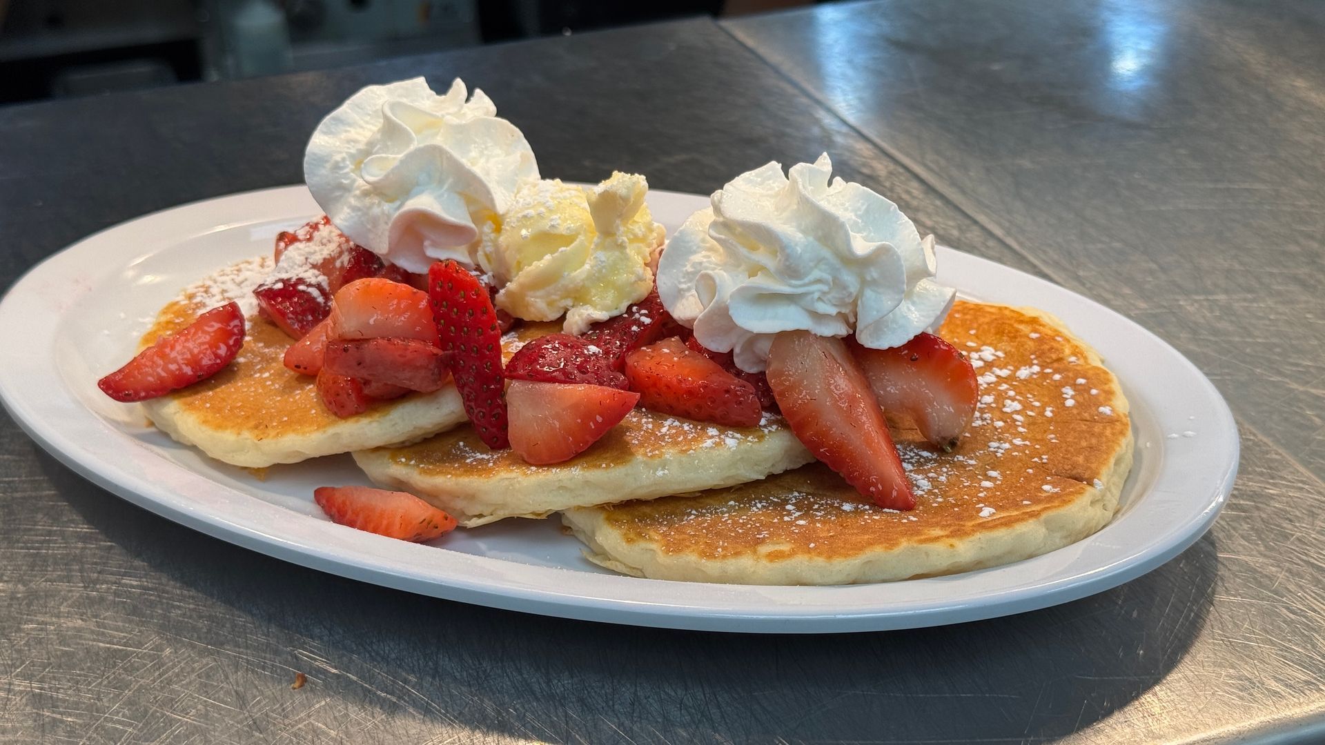 A plate of pancakes with strawberries and whipped cream on a table.