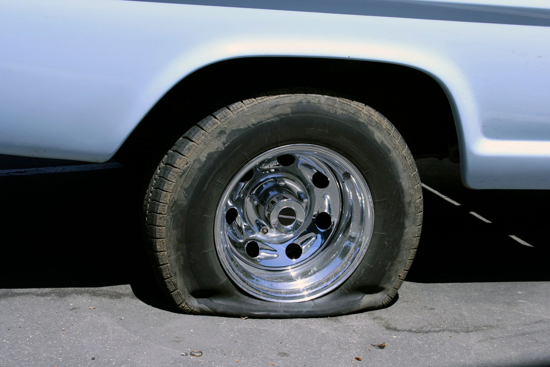 Flat tire on a light blue car, tire deflated. Chrome wheel.