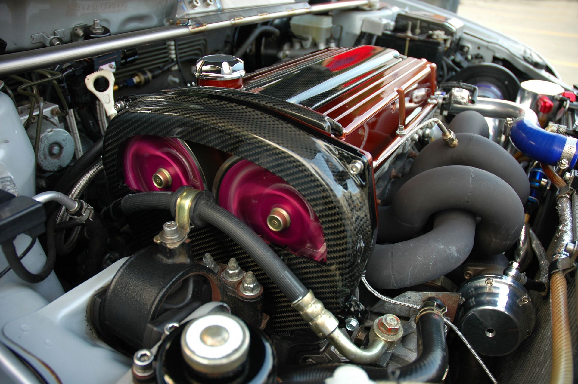 Close-up of a modified car engine bay with custom components, including a carbon fiber cover and purple pulleys.