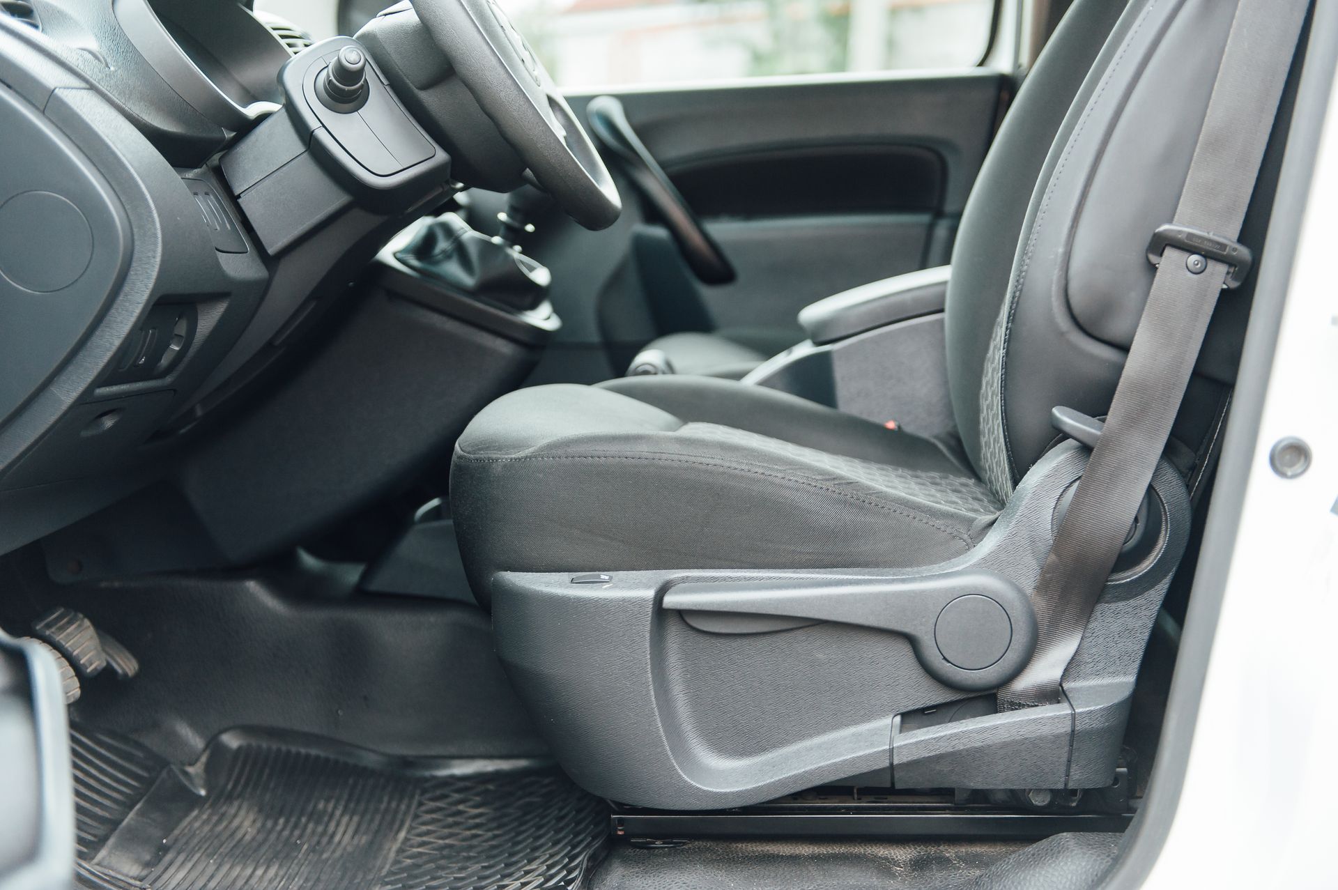 Interior view of a vehicle: driver's seat, steering wheel, and dashboard; gray and black color scheme.