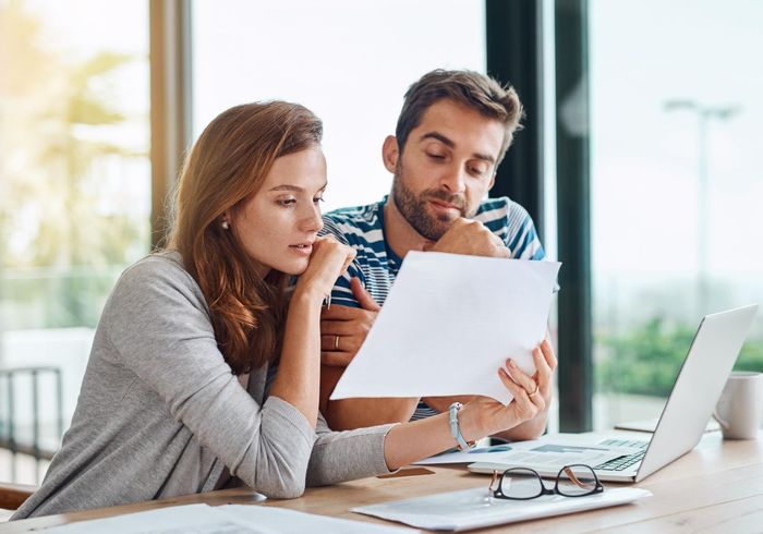Two coworkers reviewing a document at a desk with a laptop in a bright office