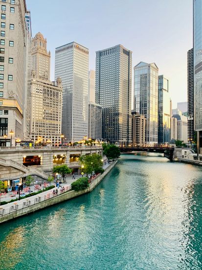 Chicago River lined with skyscrapers and a waterfront walkway at sunset