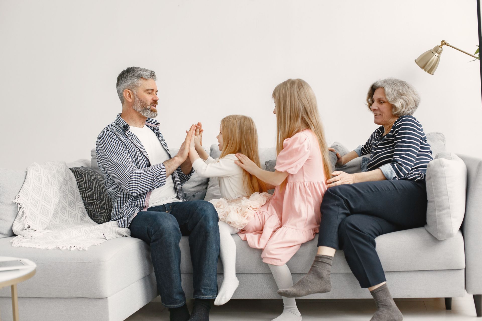 Family playing a hand-clap game on a white couch in a bright living room