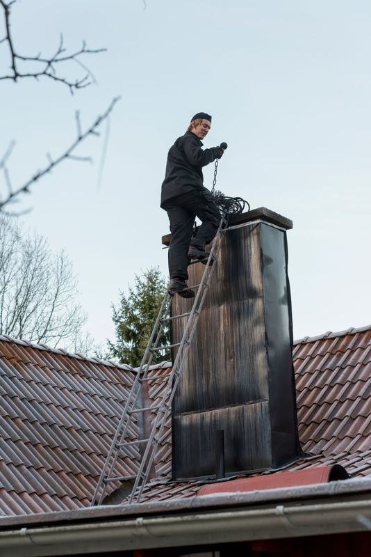 A professional chimney sweep on a ladder servicing a residential rooftop chimney A professional chimney sweep on a ladder servicing a residential rooftop chimney