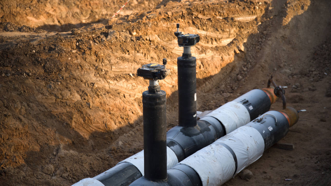 Pipes with valves in a dirt trench, likely for underground utility work.