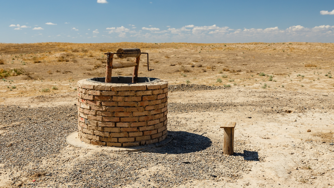 Brick well with wooden frame in a dry, barren landscape under a blue sky.