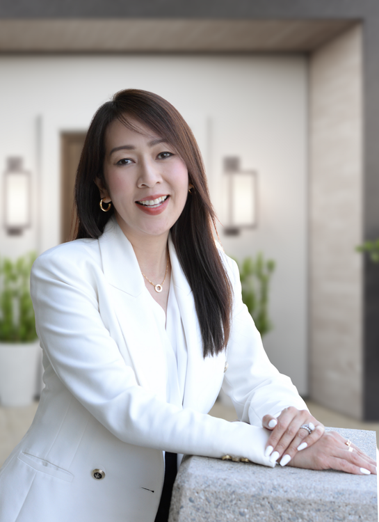 A woman is sitting at a desk with a laptop and a vase of flowers.