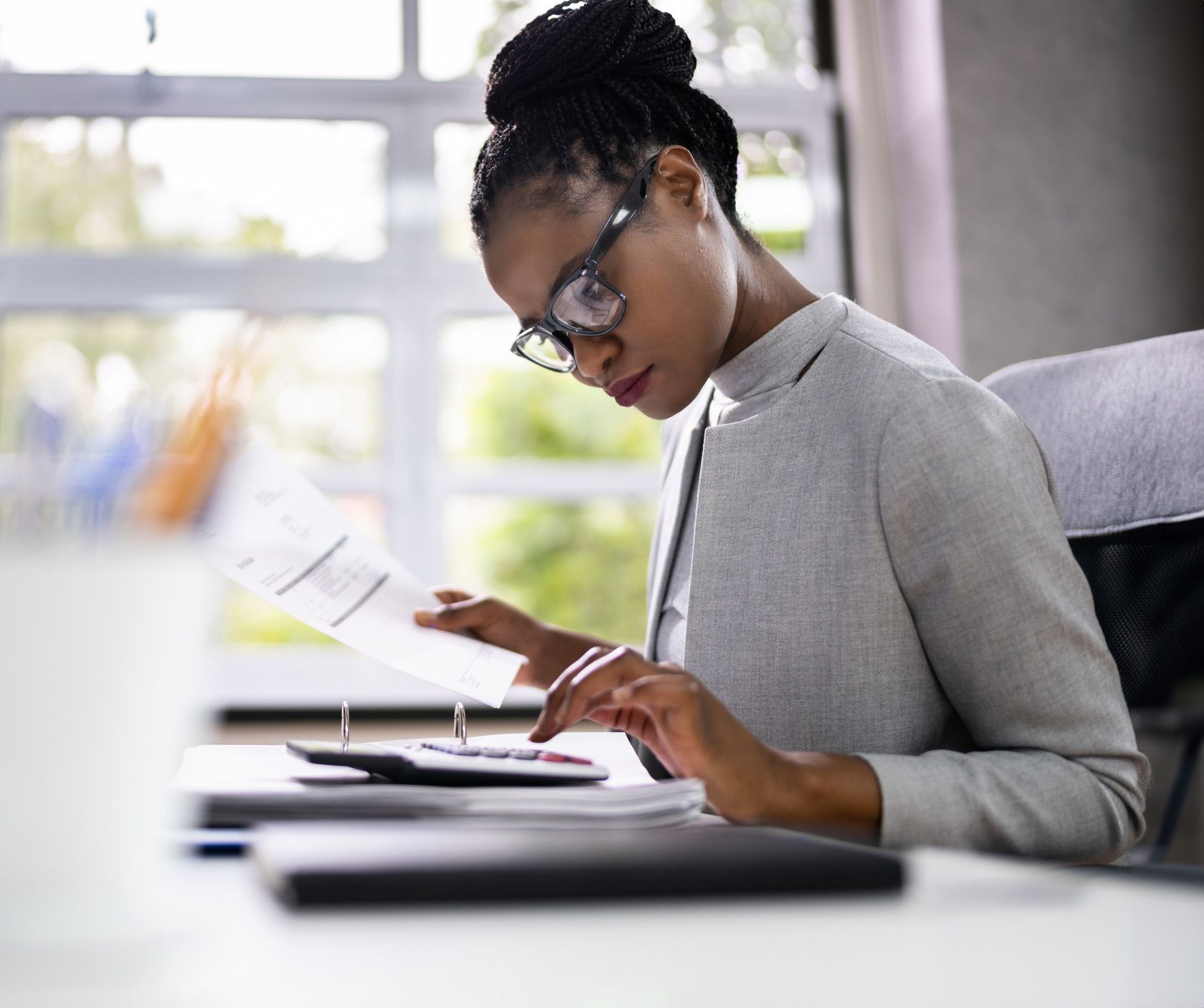 A woman is sitting at a desk with a calculator and a piece of paper.