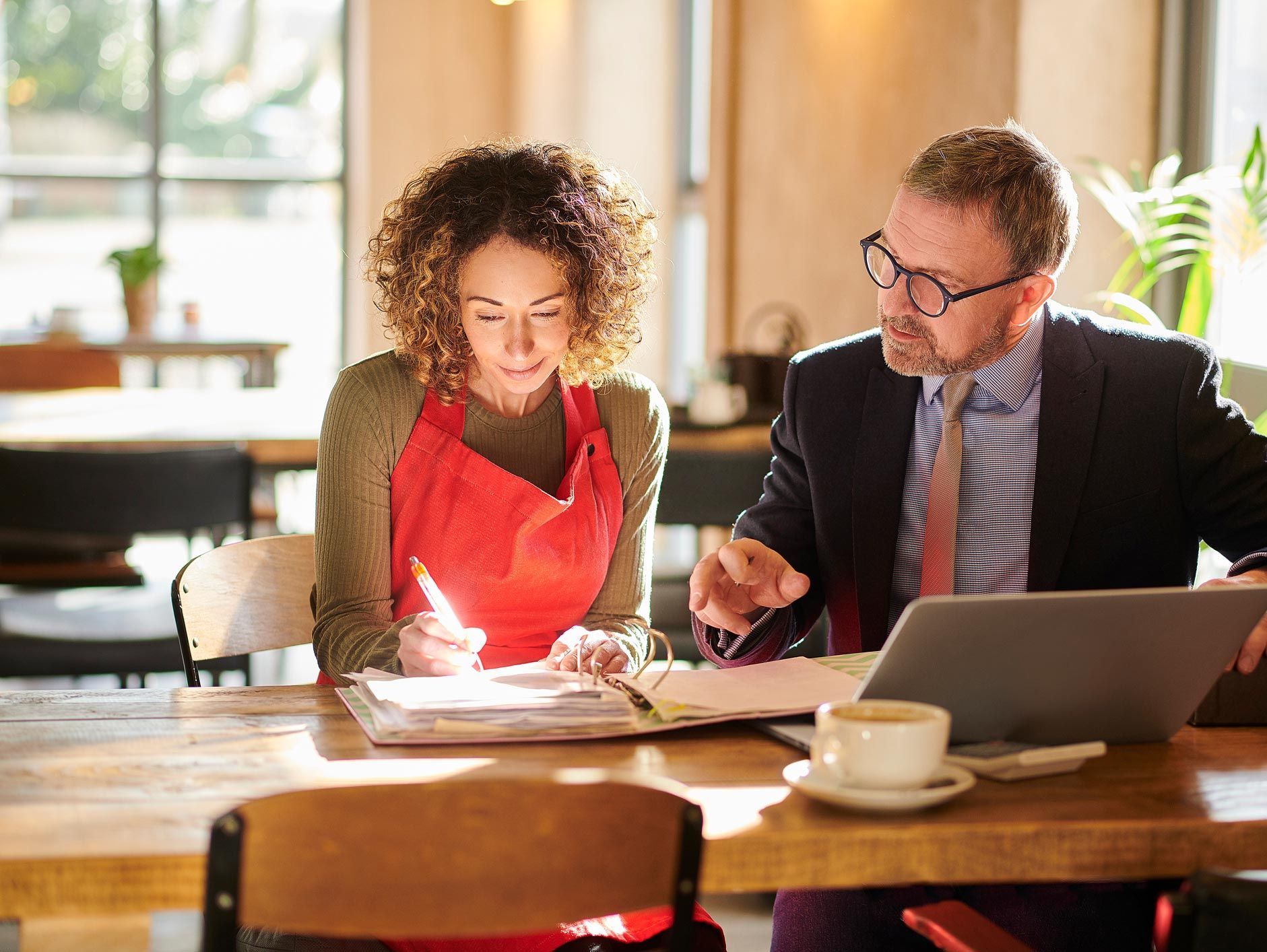 A man and a woman are sitting at a table looking at a laptop.