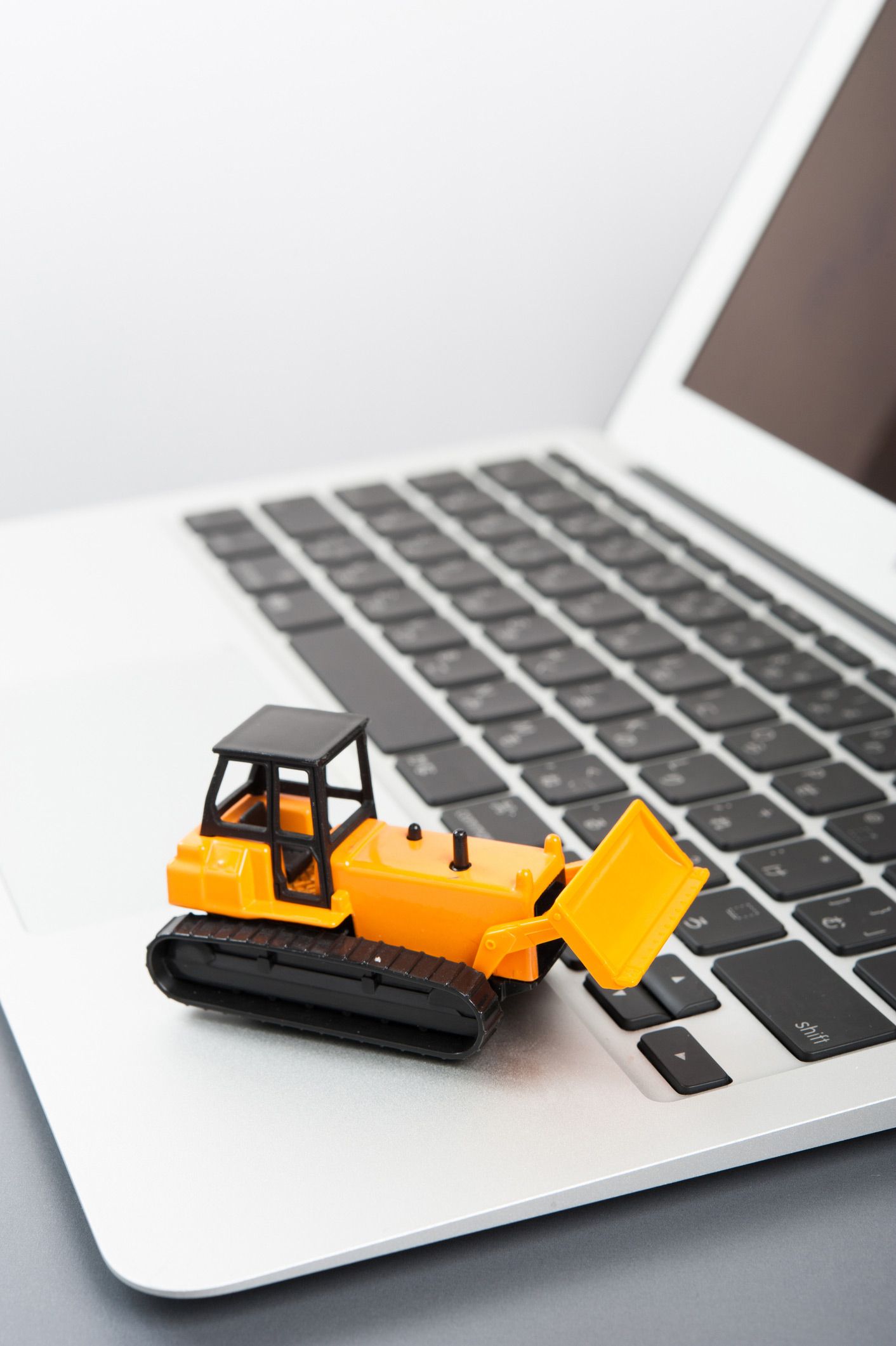 A toy bulldozer is sitting on top of a laptop keyboard