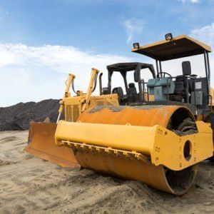 A bulldozer and a road roller are sitting on top of a dirt field.