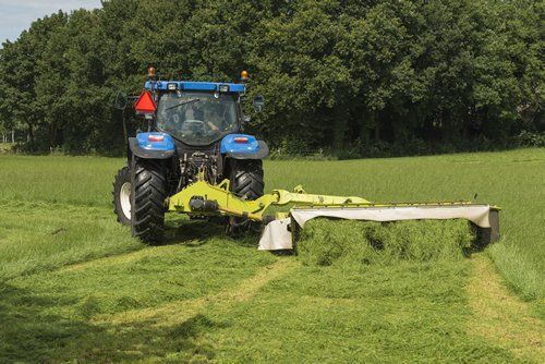 A blue tractor is cutting grass in a field.