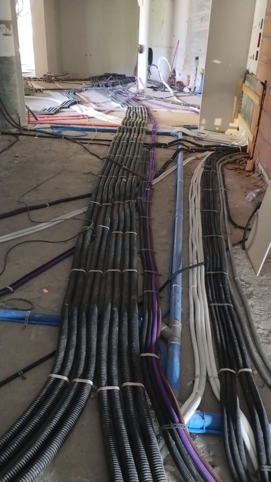 Cavi protettivi giacciono su un pavimento di cemento in un cantiere. Sono visibili vari colori e lunghezze.