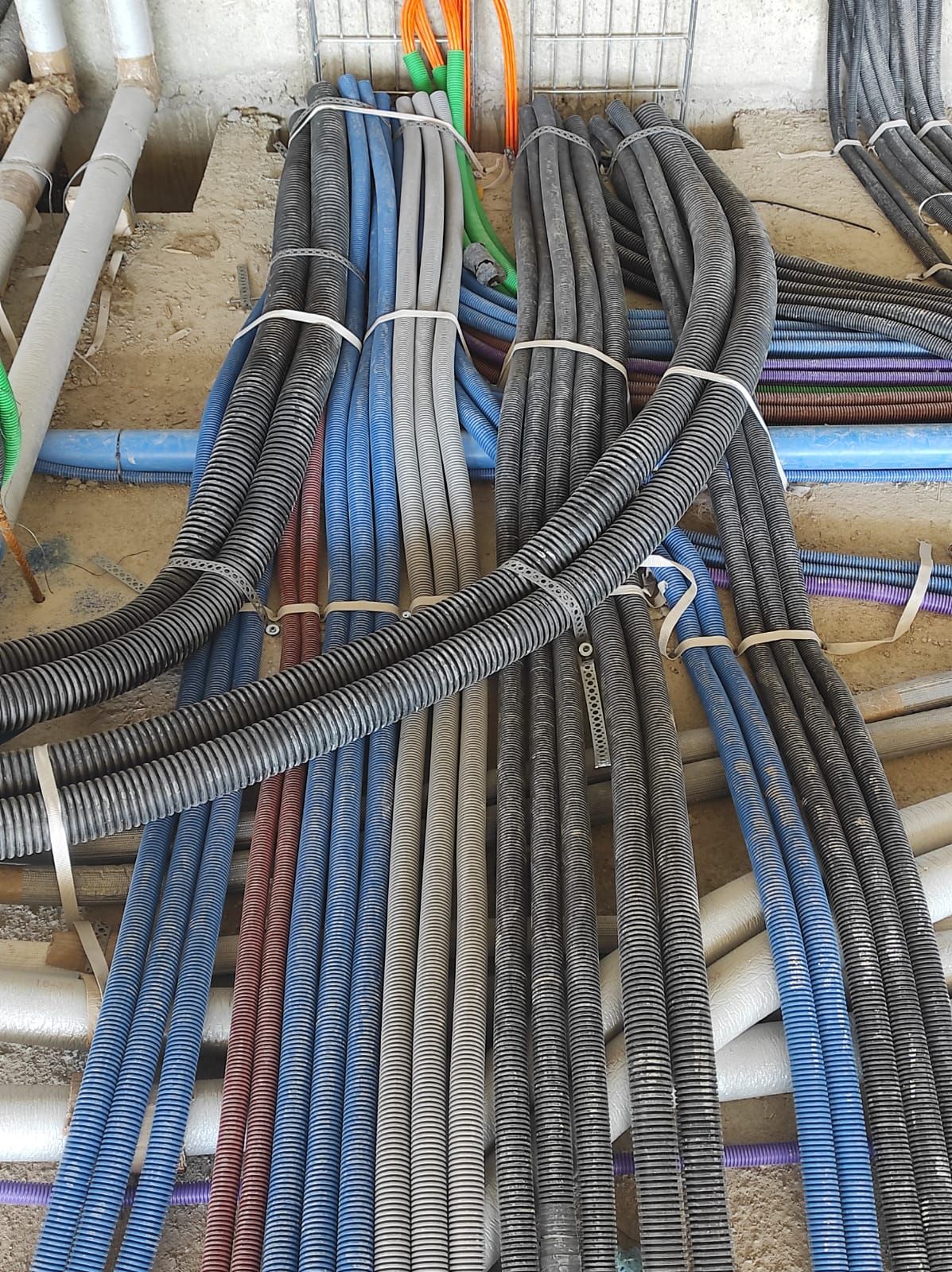 Fasci di cavi elettrici corrugati neri, grigi e blu legati insieme, alcuni dei quali poggiano su una superficie di cemento.