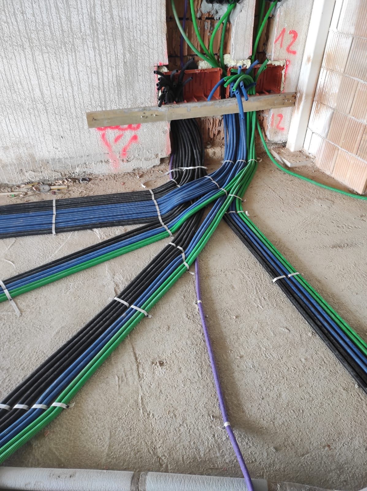 Cavi di diversi colori (blu, verde, nero) raggruppati e fissati su un pavimento di cemento vicino a un muro.