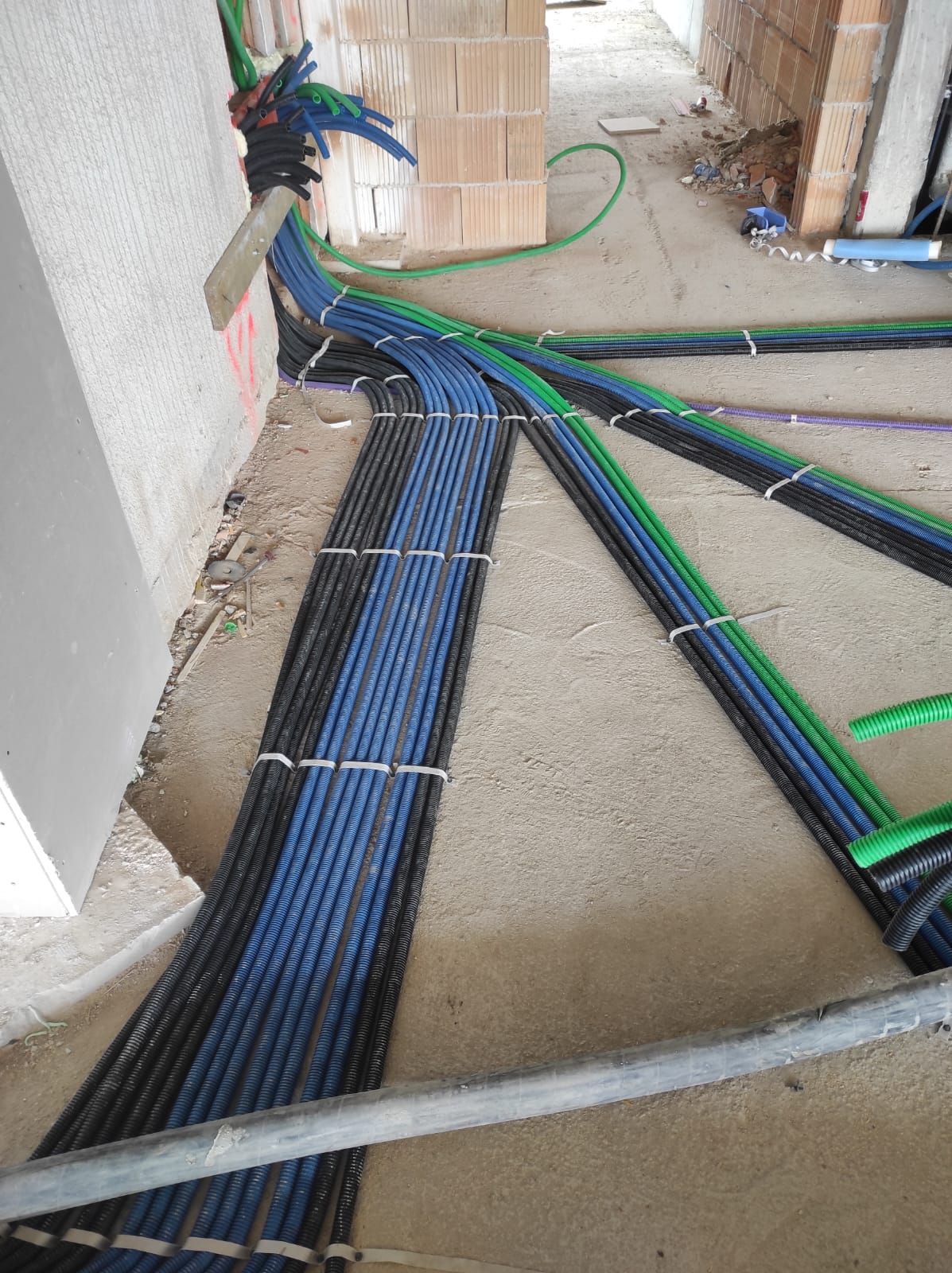 Fasci di tubi blu, neri e verdi sul pavimento di un cantiere edile, fissati con fascette bianche.