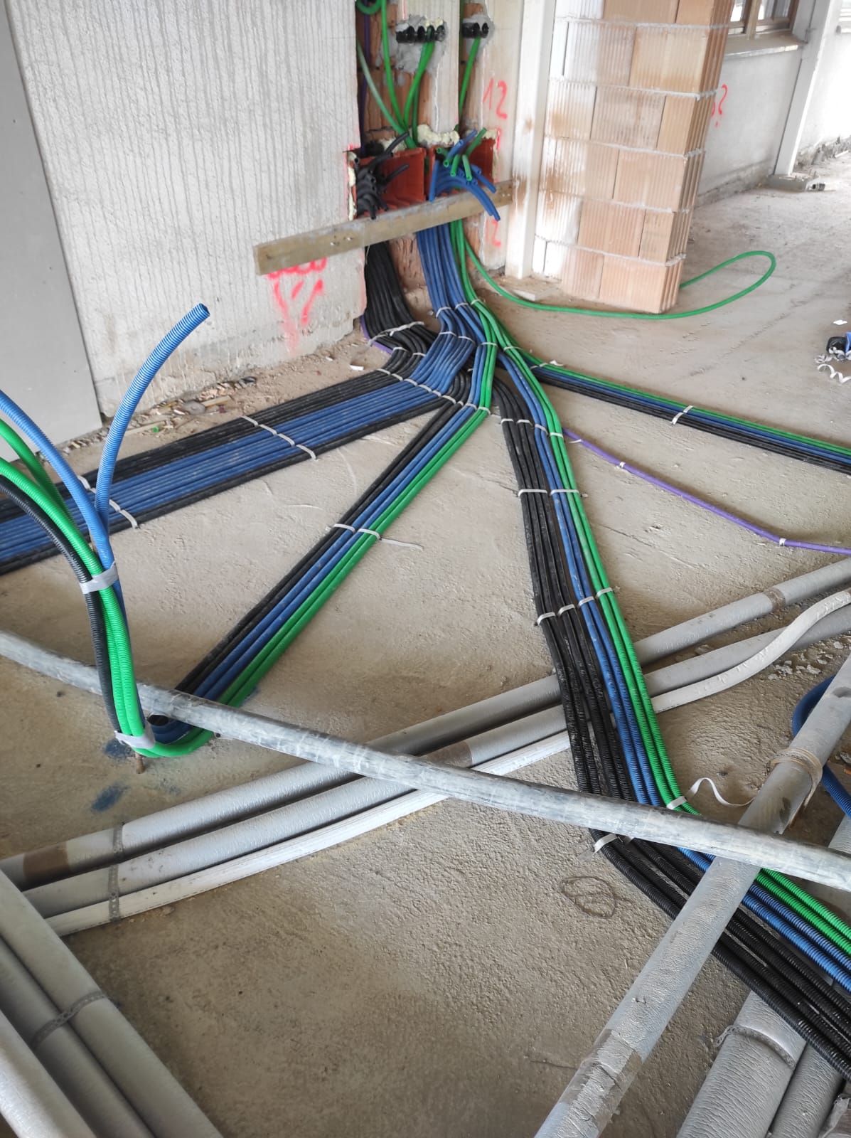 Durante la costruzione, cavi elettrici e condotti di vari colori giacciono su un pavimento di cemento.