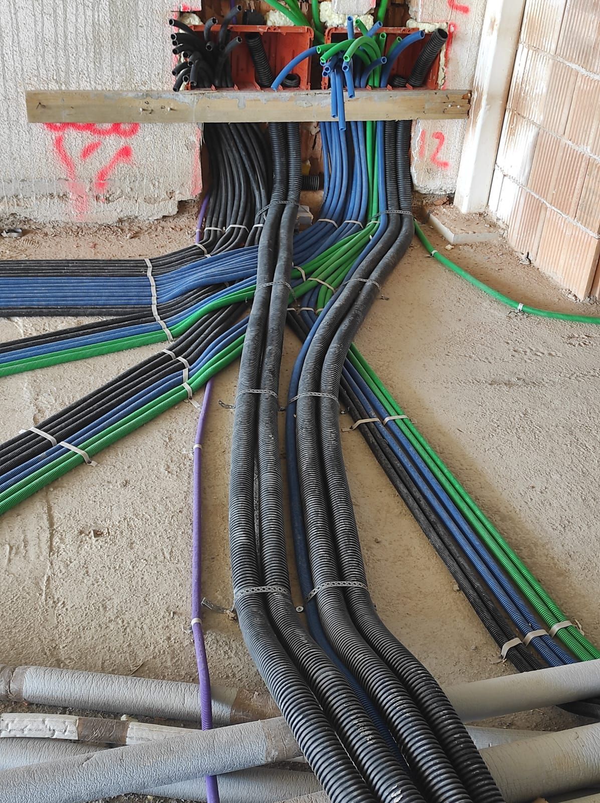 Fasci di cavi elettrici, per lo più blu e neri, attraversano un muro di cemento.