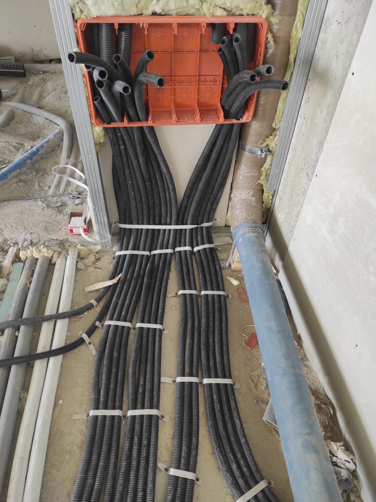 Installazione del cablaggio elettrico, scatola di giunzione arancione con condotti neri, cavi raggruppati e fissati con fascette, cantiere.