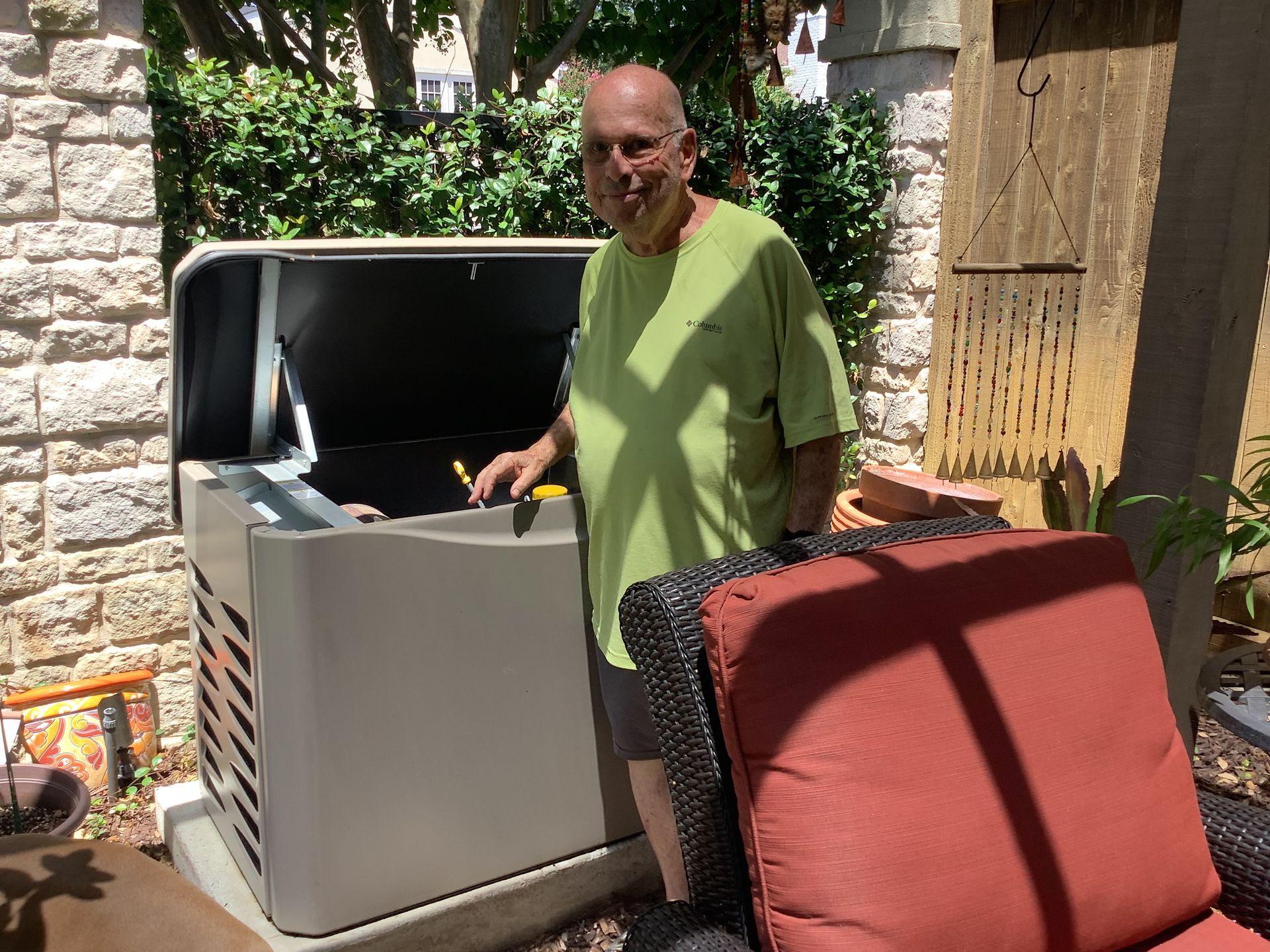 Man near a generator in a courtyard, light green shirt, brick and stone background.