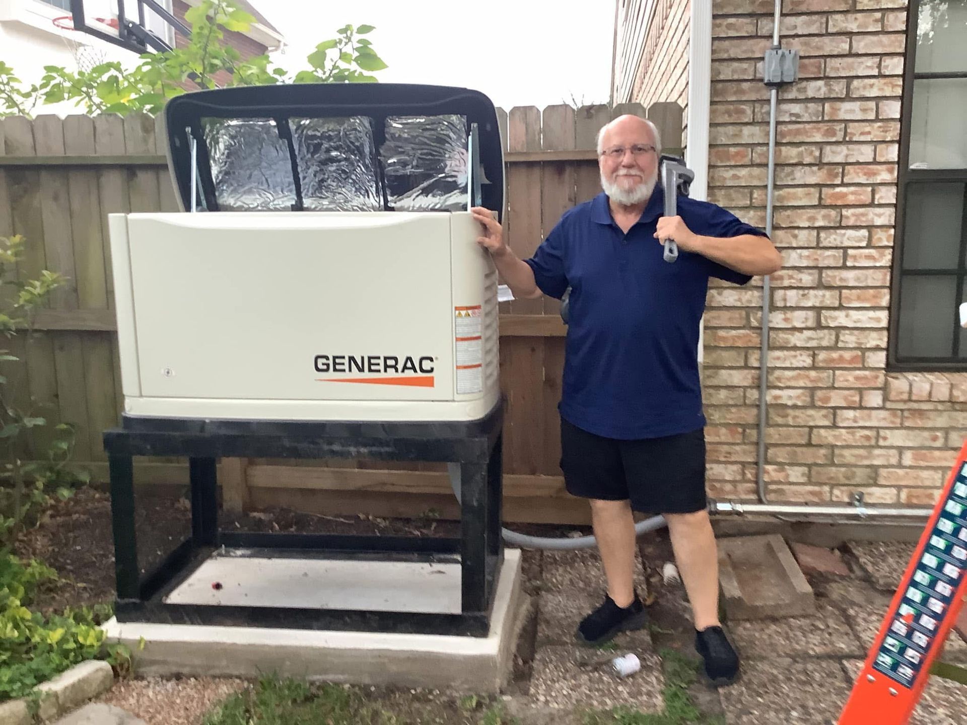Man with a hammer stands next to a Generac generator on a brick patio.