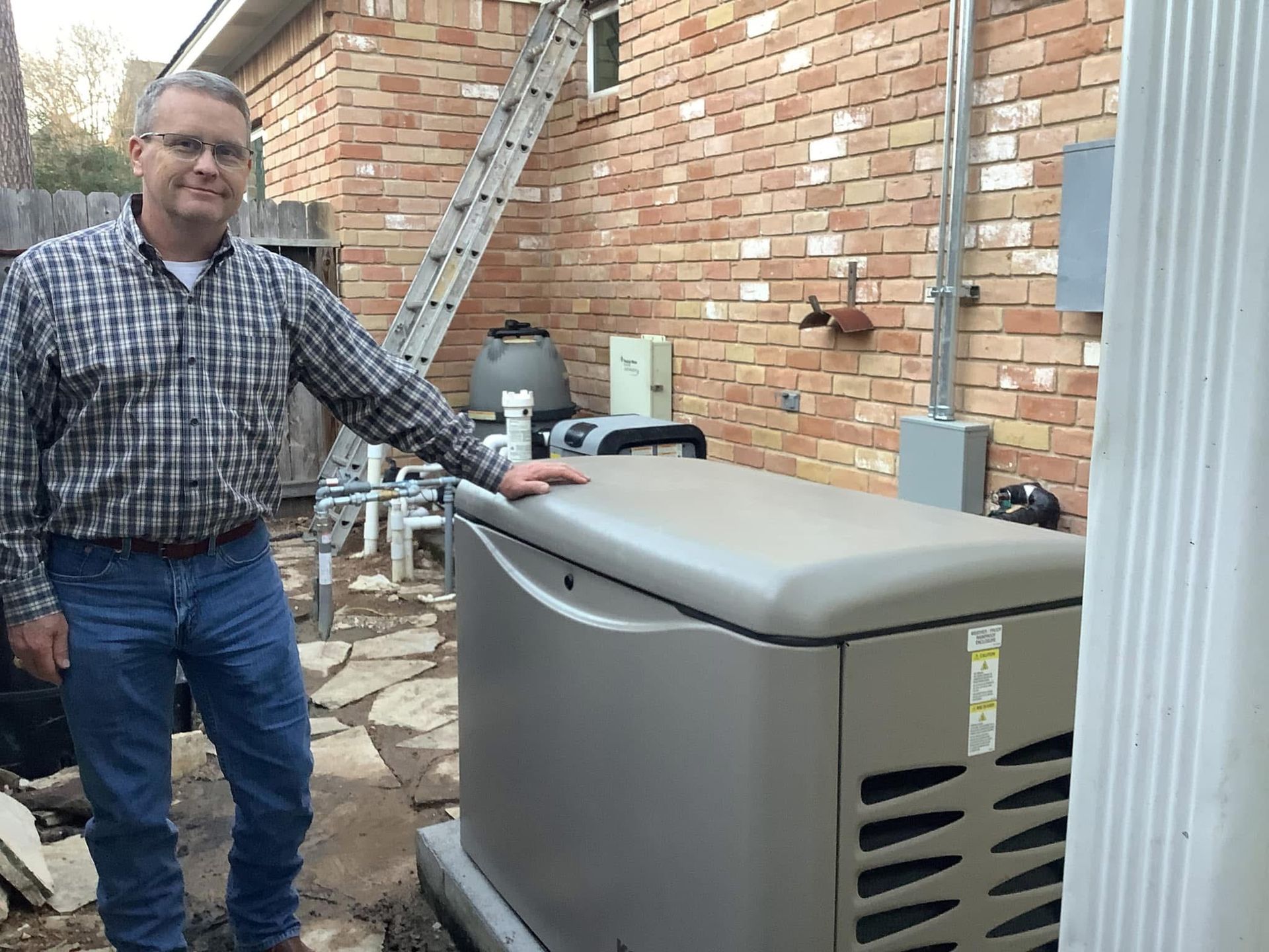 Man standing by a large, beige generator near a brick wall. He is smiling and wearing casual clothes.