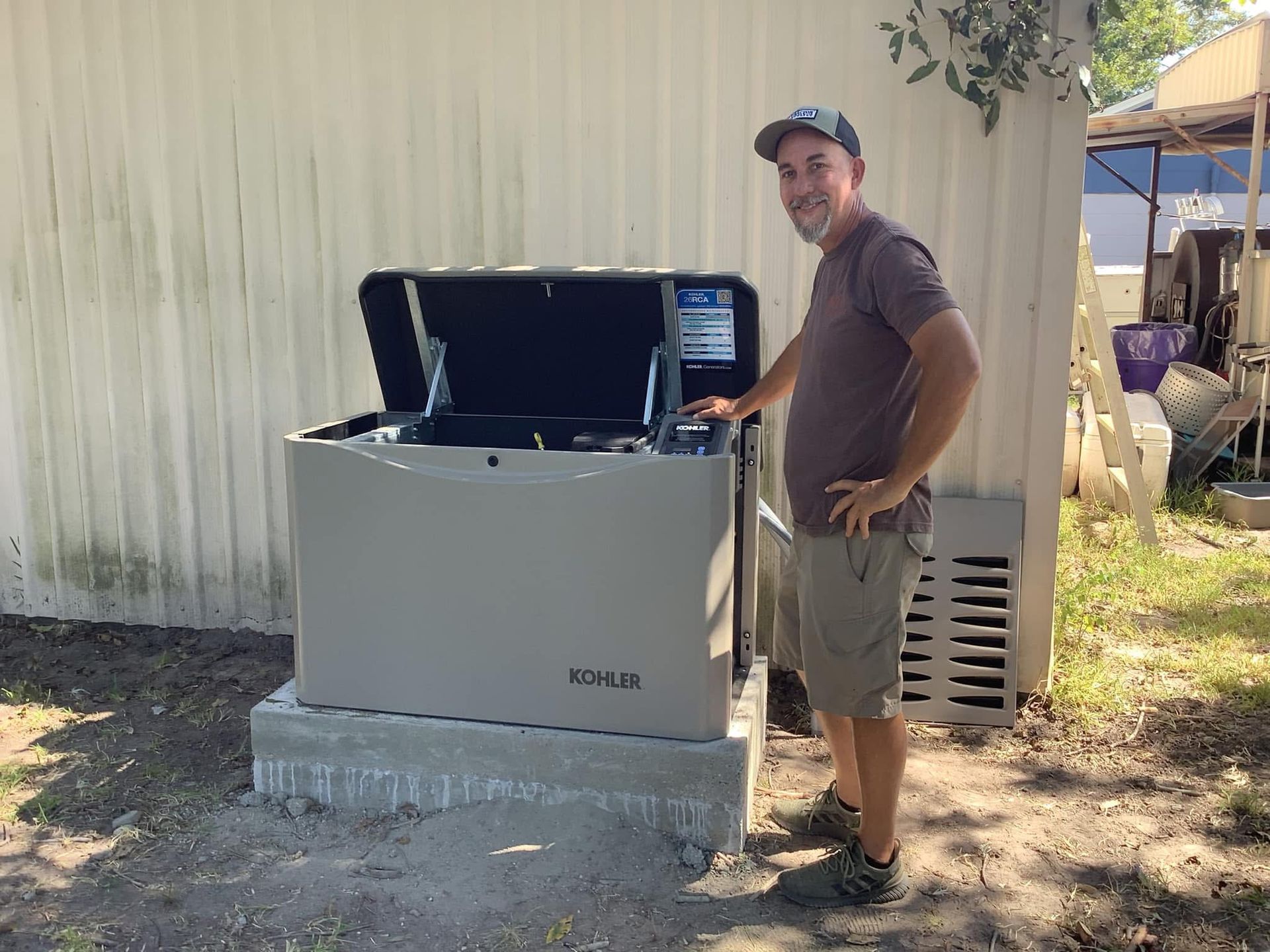 Man stands beside a tan generator on a concrete base outdoors. The generator's top is open.
