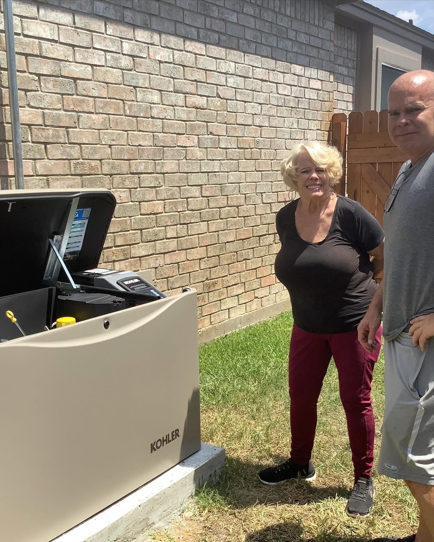 Woman and man stand near a beige home generator, in front of a brick wall.
