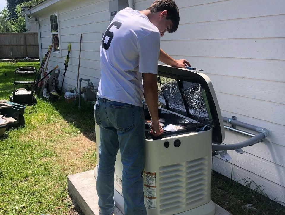 Man in a white shirt and jeans working on a generator outside a house.