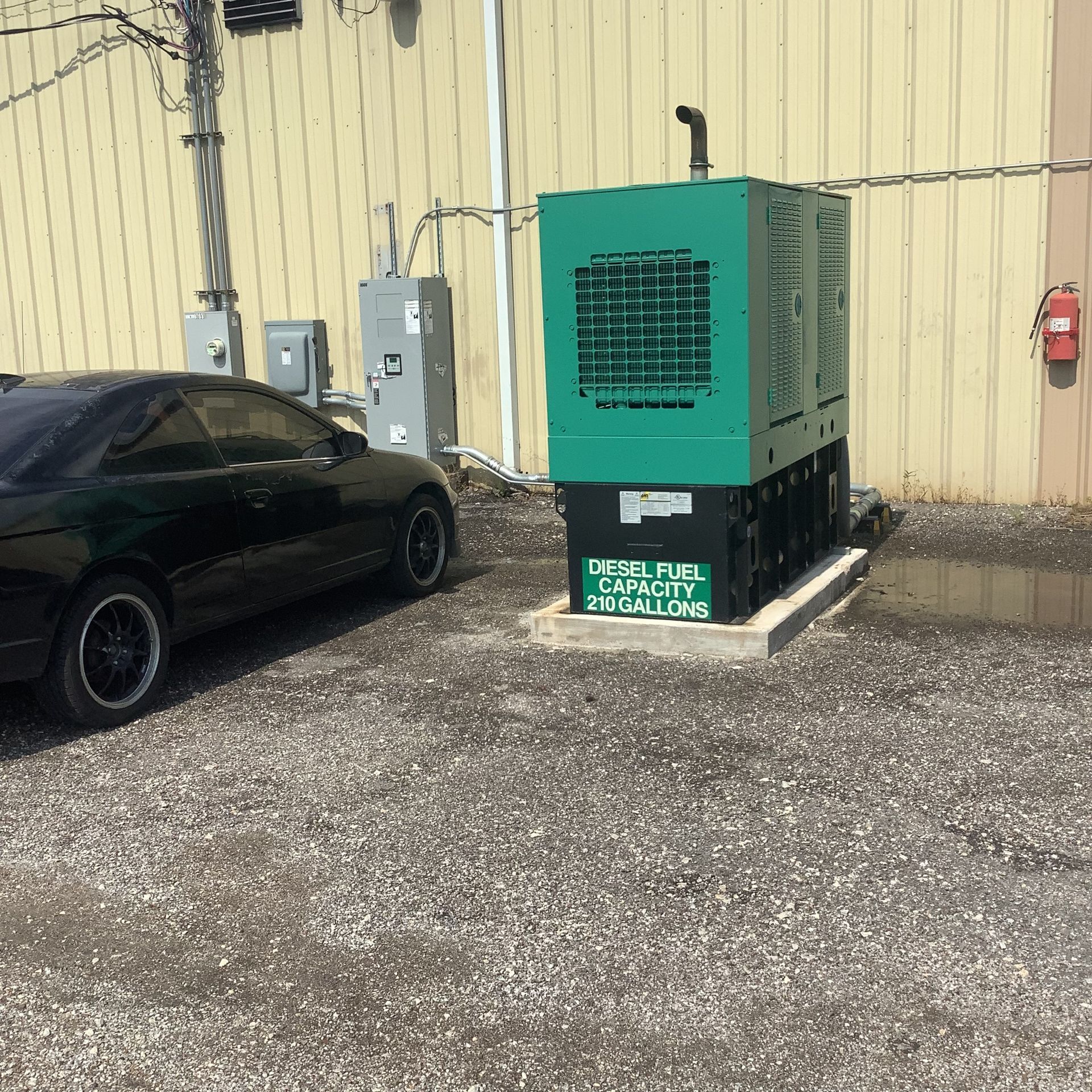 Green generator outside a building next to a black car.