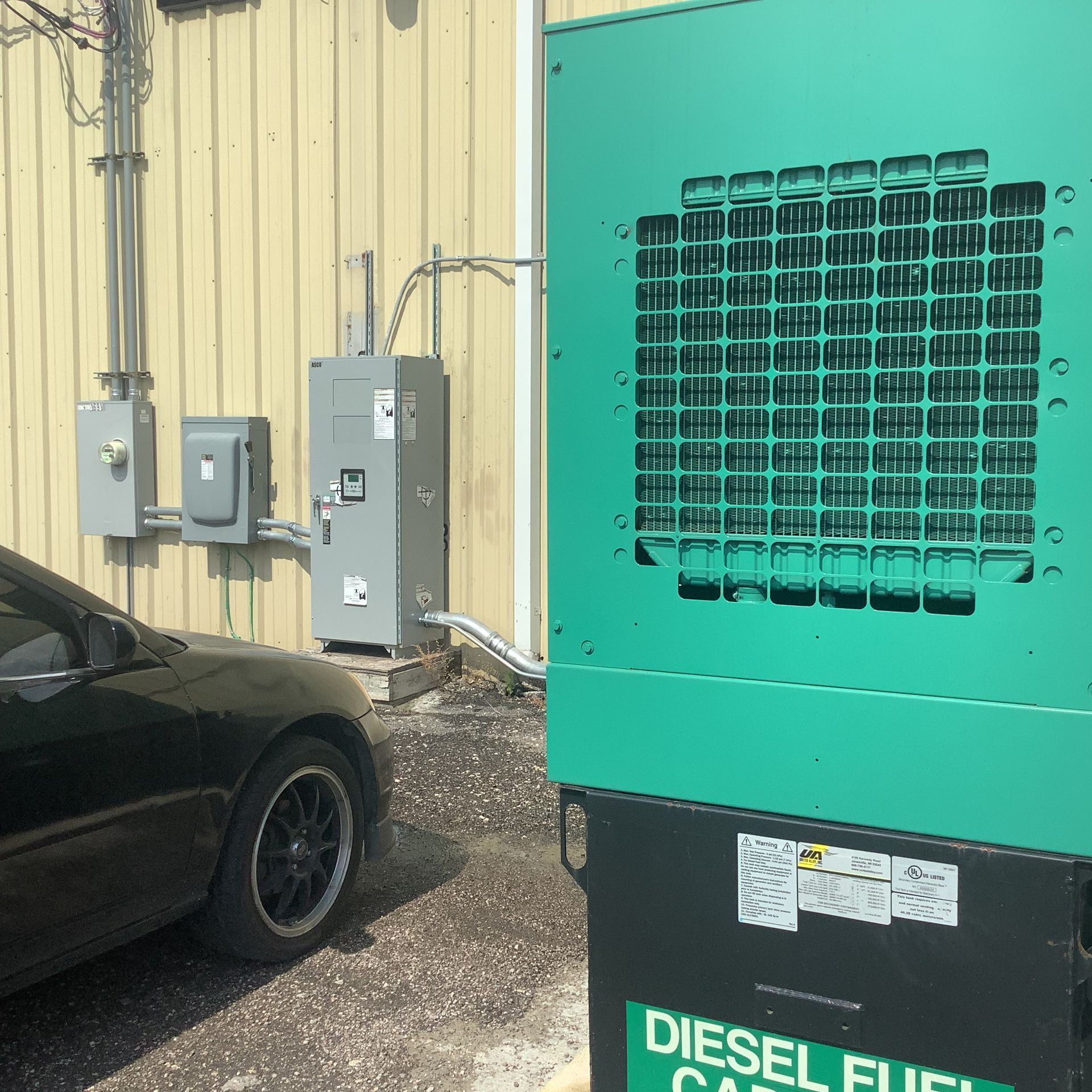 Black car parked near green generator with electrical equipment on a building.