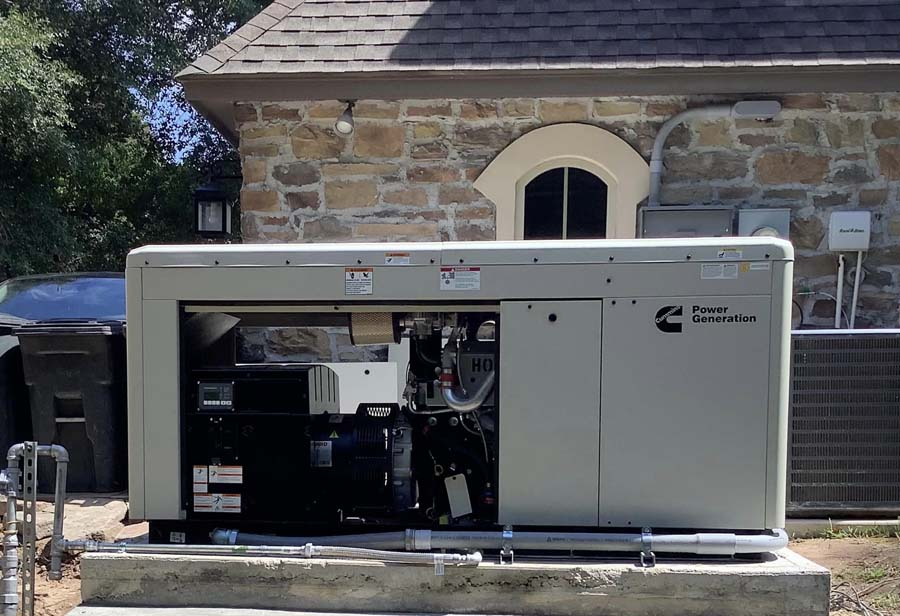 Exterior of a beige Cummins generator near a stone building.