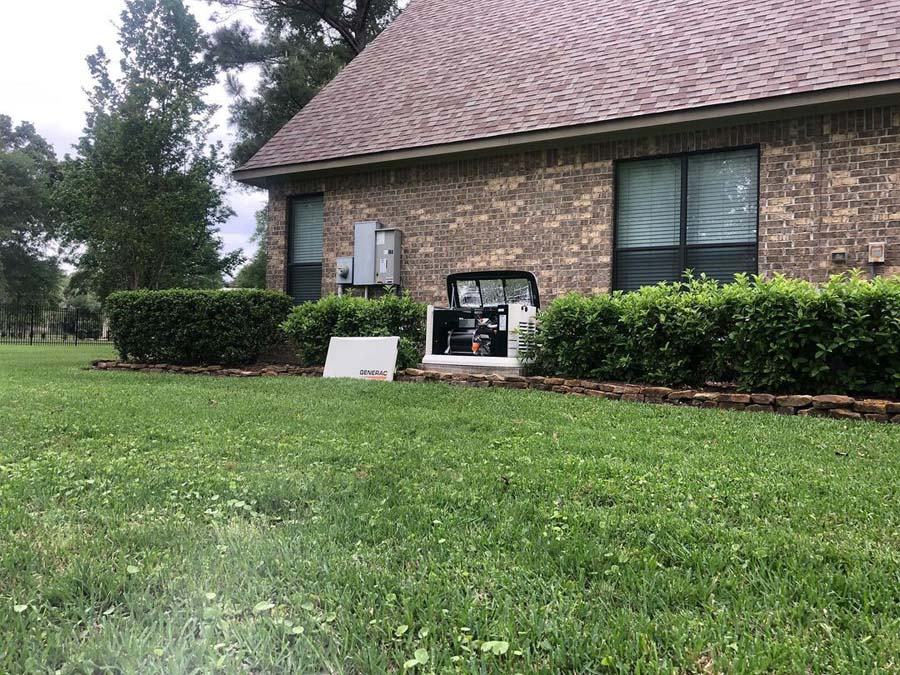 A brick house with a generator outside. Bushes and lawn surround the building.