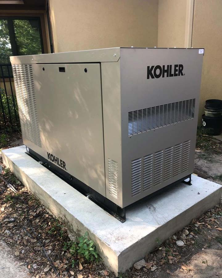 Kohler generator on a concrete pad. Gray metal enclosure, black lettering. Outdoors.