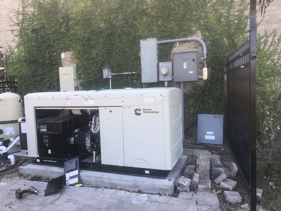 A beige Cummins generator outside, electrical boxes on wall, a partially visible pool and fence.